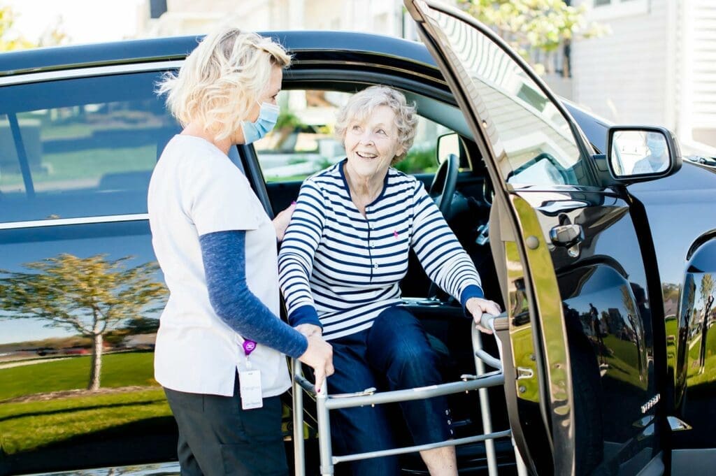 Caregiver helping lady with walker out of car